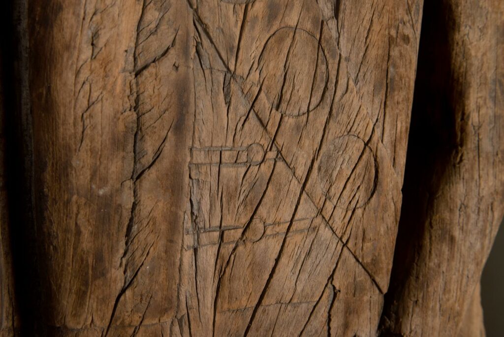 Paiwan tribe: massive 19th-century ancestral panel measuring over 2.5 meters, depicting a hunter wearing a Paiwan-style hat and holding a knife and a spear at his side. The carvings on his torso suggest he is dressed in a ceremonial vest and the shoulder belt traditionally worn by nobles. Due to its size, this panel was likely the central piece of the house.