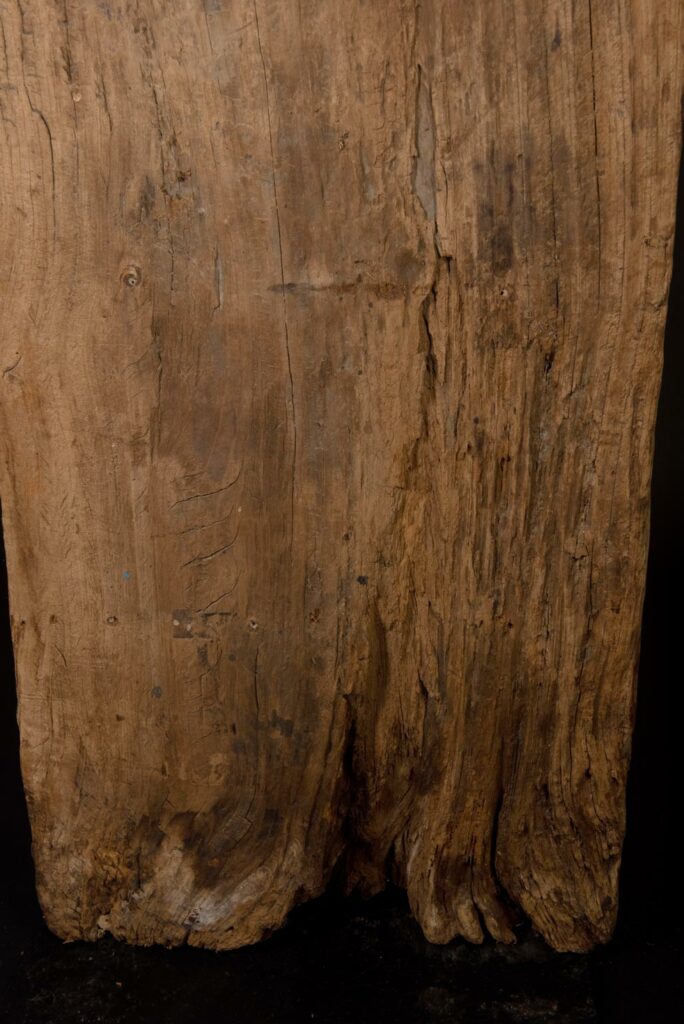 Paiwan tribe: massive 19th-century ancestral panel measuring over 2.5 meters, depicting a hunter wearing a Paiwan-style hat and holding a knife and a spear at his side. The carvings on his torso suggest he is dressed in a ceremonial vest and the shoulder belt traditionally worn by nobles. Due to its size, this panel was likely the central piece of the house.