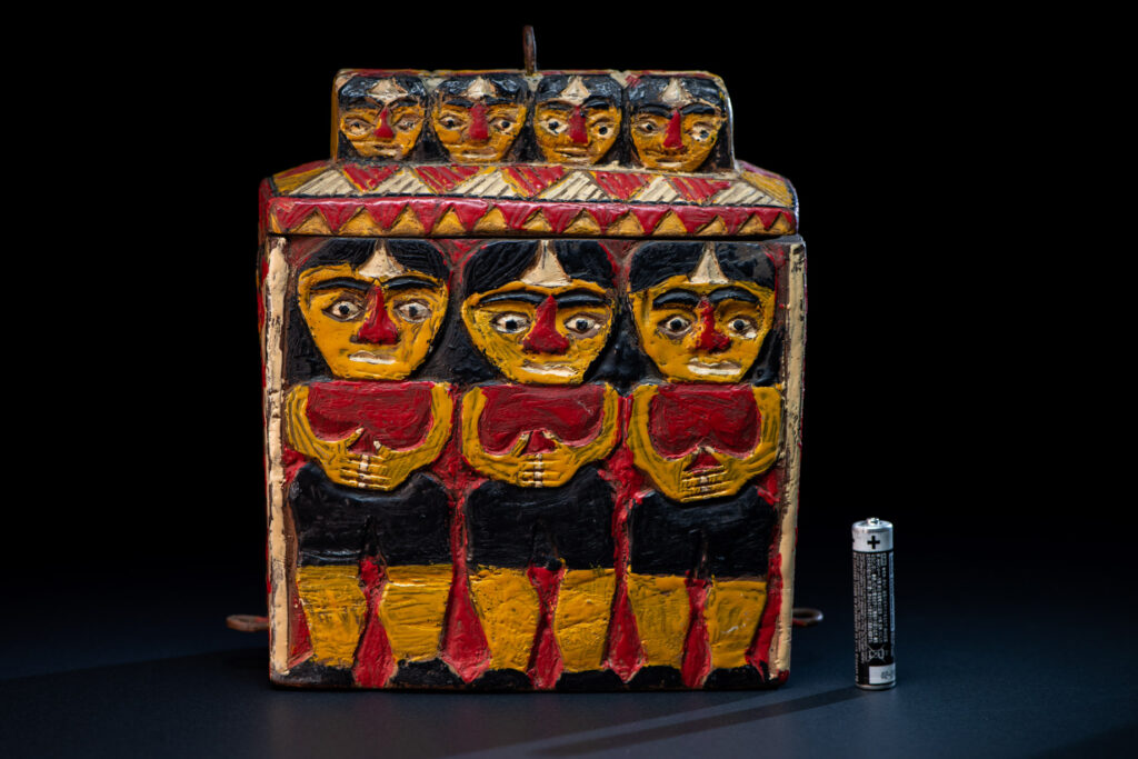 Paiwan tribe shaman box features a sliding lid, carved with human heads and painted in red, yellow, white, and black. Standing figure is carved on the other sides.