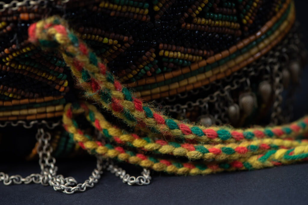 Women's headdress from the Paiwan tribe, made of green, yellow, red, and black beads arranged in geometric patterns, surrounded by chains and topped with boar tusks.