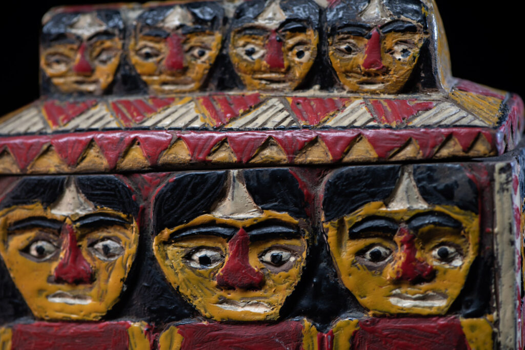 Paiwan tribe shaman box features a sliding lid, carved with human heads and painted in red, yellow, white, and black. Standing figure is carved on the other sides.
