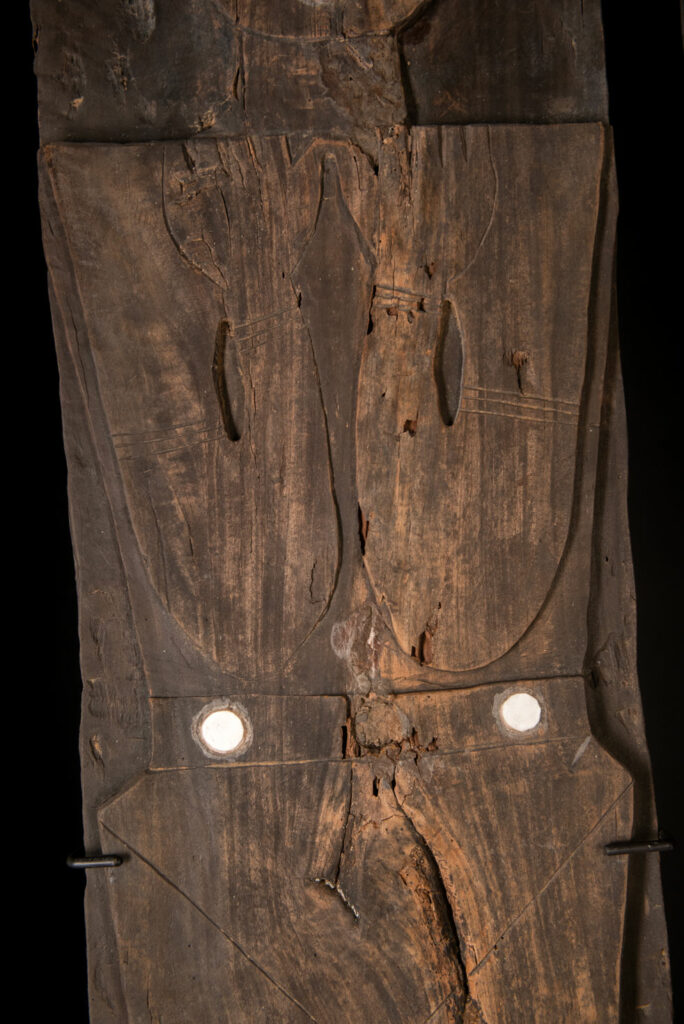 Pair of ancestor panels from the Paiwan tribe, depicting a male and a female figure, both wearing feathered headdresses — symbols of valor and vigor. The panels are inlaid with porcelain circles at the eyes, mouth, and waist, representing the ceremonial belts they wear.