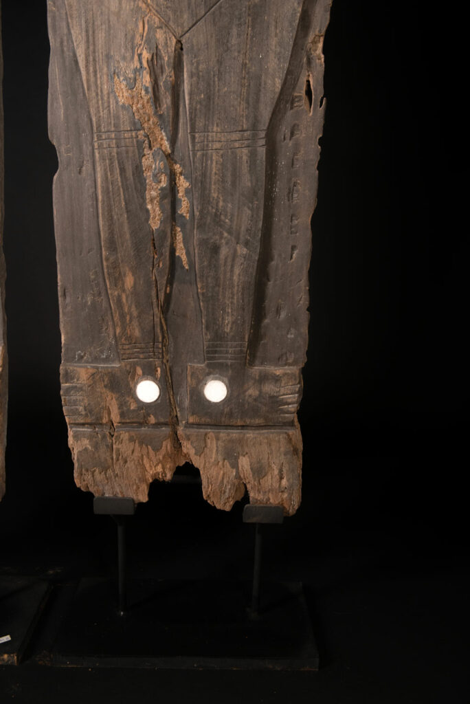 Pair of ancestor panels from the Paiwan tribe, depicting a male and a female figure, both wearing feathered headdresses — symbols of valor and vigor. The panels are inlaid with porcelain circles at the eyes, mouth, and waist, representing the ceremonial belts they wear.