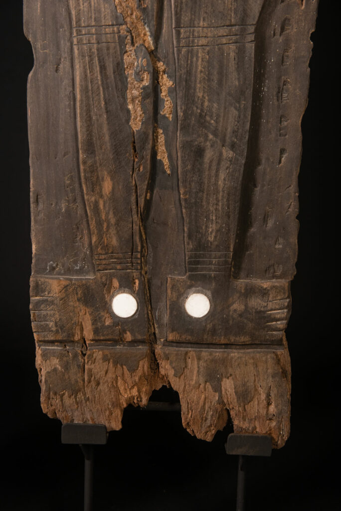 Pair of ancestor panels from the Paiwan tribe, depicting a male and a female figure, both wearing feathered headdresses — symbols of valor and vigor. The panels are inlaid with porcelain circles at the eyes, mouth, and waist, representing the ceremonial belts they wear.
