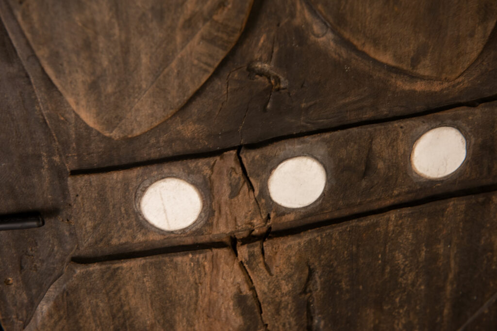 Pair of ancestor panels from the Paiwan tribe, depicting a male and a female figure, both wearing feathered headdresses — symbols of valor and vigor. The panels are inlaid with porcelain circles at the eyes, mouth, and waist, representing the ceremonial belts they wear.