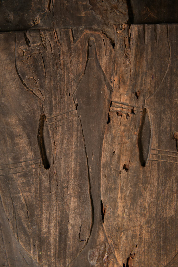 Pair of ancestor panels from the Paiwan tribe, depicting a male and a female figure, both wearing feathered headdresses — symbols of valor and vigor. The panels are inlaid with porcelain circles at the eyes, mouth, and waist, representing the ceremonial belts they wear.