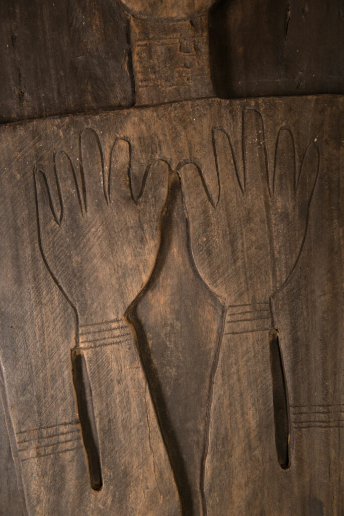 Pair of ancestor panels from the Paiwan tribe, depicting a male and a female figure, both wearing feathered headdresses — symbols of valor and vigor. The panels are inlaid with porcelain circles at the eyes, mouth, and waist, representing the ceremonial belts they wear.