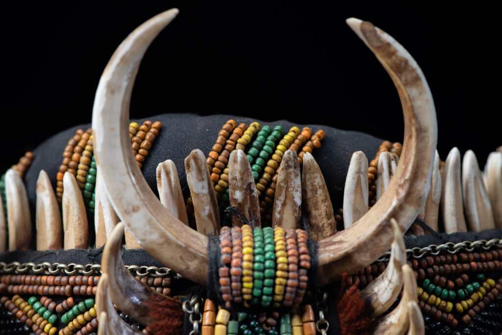 Women's headdress from the Paiwan tribe, made of green, yellow, red, and black beads arranged in geometric patterns, surrounded by chains and topped with boar tusks.
