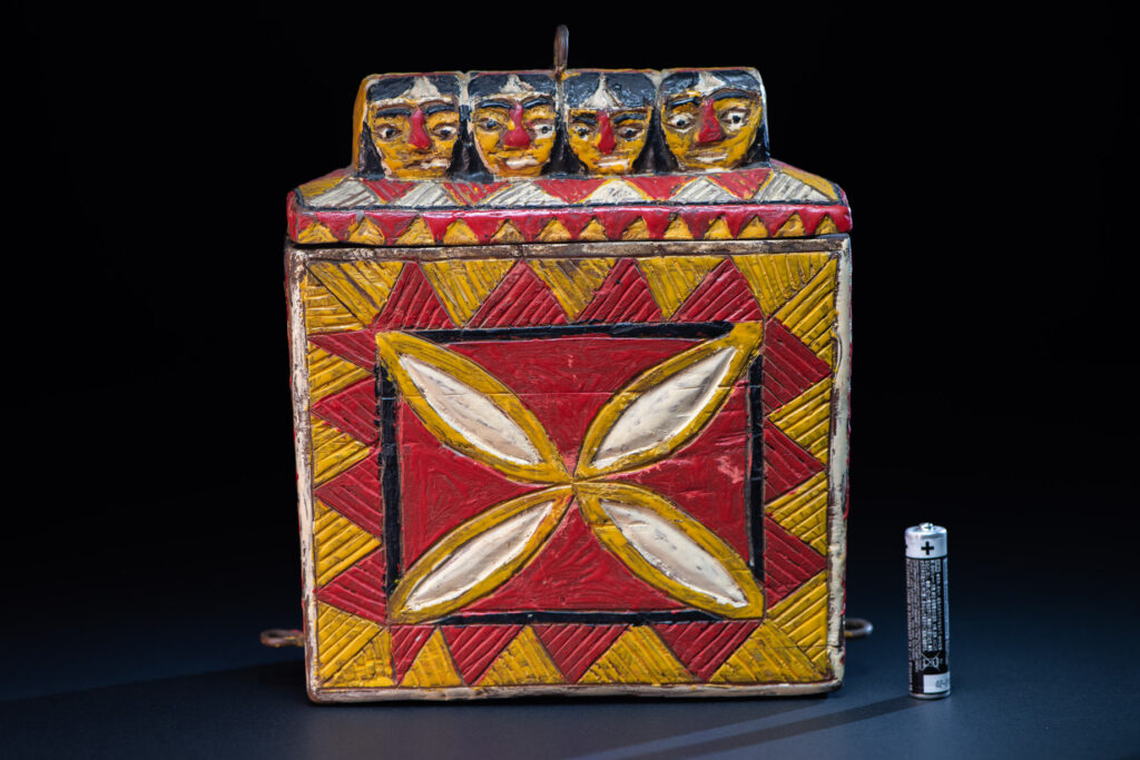Paiwan tribe shaman box features a sliding lid, carved with human heads and painted in red, yellow, white, and black. Standing figure is carved on the other sides.