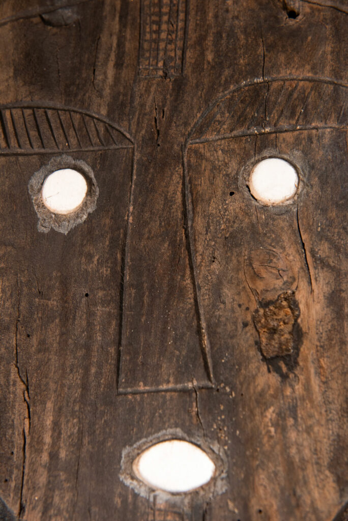 Pair of ancestor panels from the Paiwan tribe, depicting a male and a female figure, both wearing feathered headdresses — symbols of valor and vigor. The panels are inlaid with porcelain circles at the eyes, mouth, and waist, representing the ceremonial belts they wear.