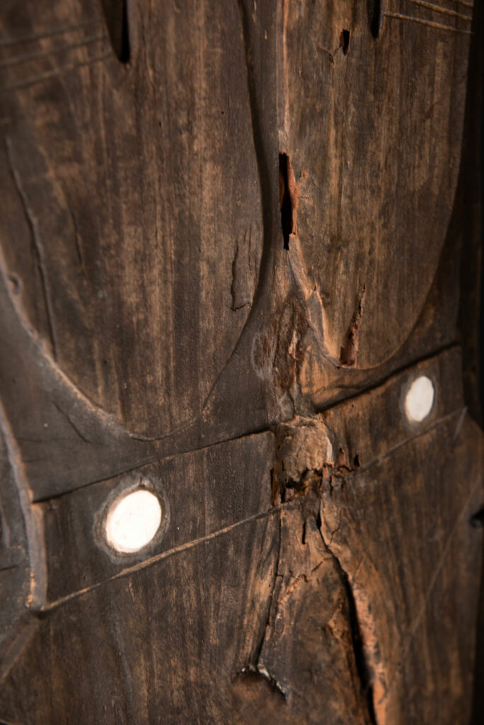 Pair of ancestor panels from the Paiwan tribe, depicting a male and a female figure, both wearing feathered headdresses — symbols of valor and vigor. The panels are inlaid with porcelain circles at the eyes, mouth, and waist, representing the ceremonial belts they wear.