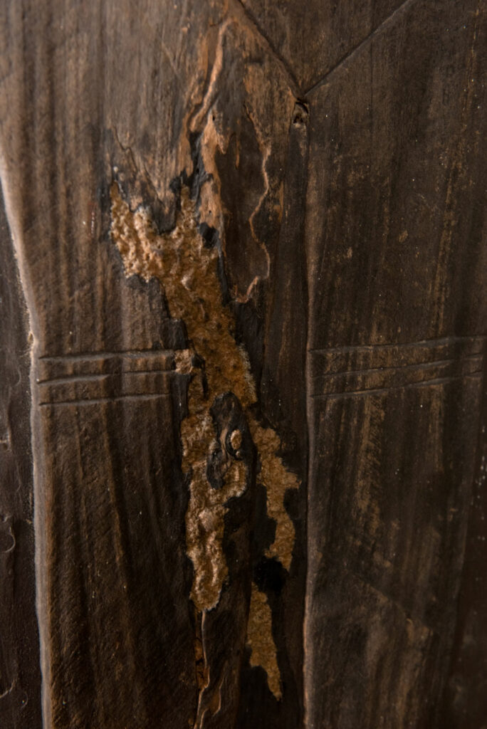 Pair of ancestor panels from the Paiwan tribe, depicting a male and a female figure, both wearing feathered headdresses — symbols of valor and vigor. The panels are inlaid with porcelain circles at the eyes, mouth, and waist, representing the ceremonial belts they wear.