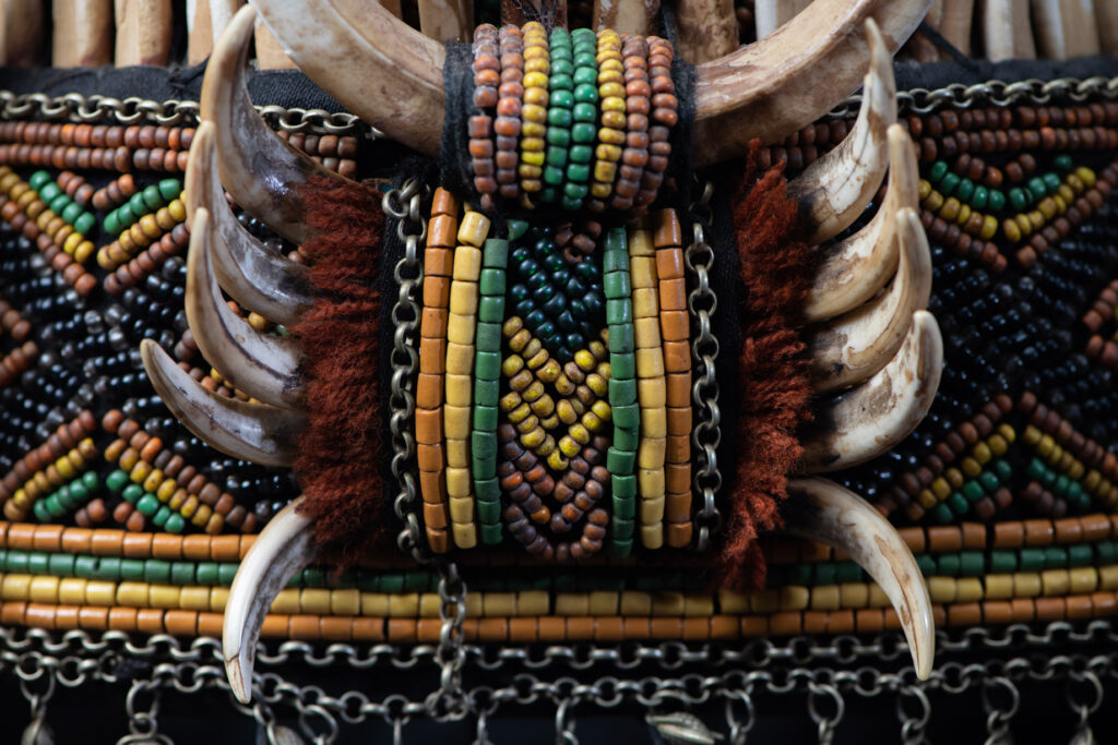 Women's headdress from the Paiwan tribe, made of green, yellow, red, and black beads arranged in geometric patterns, surrounded by chains and topped with boar tusks.
