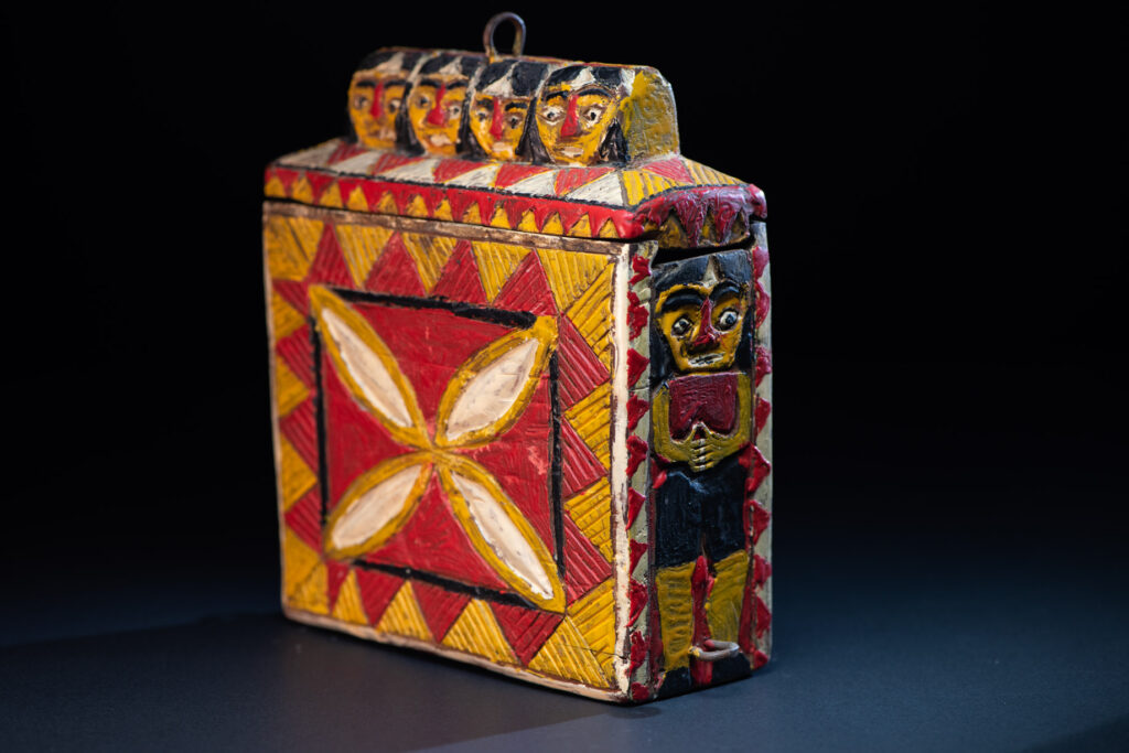 Paiwan tribe shaman box features a sliding lid, carved with human heads and painted in red, yellow, white, and black. Standing figure is carved on the other sides.
