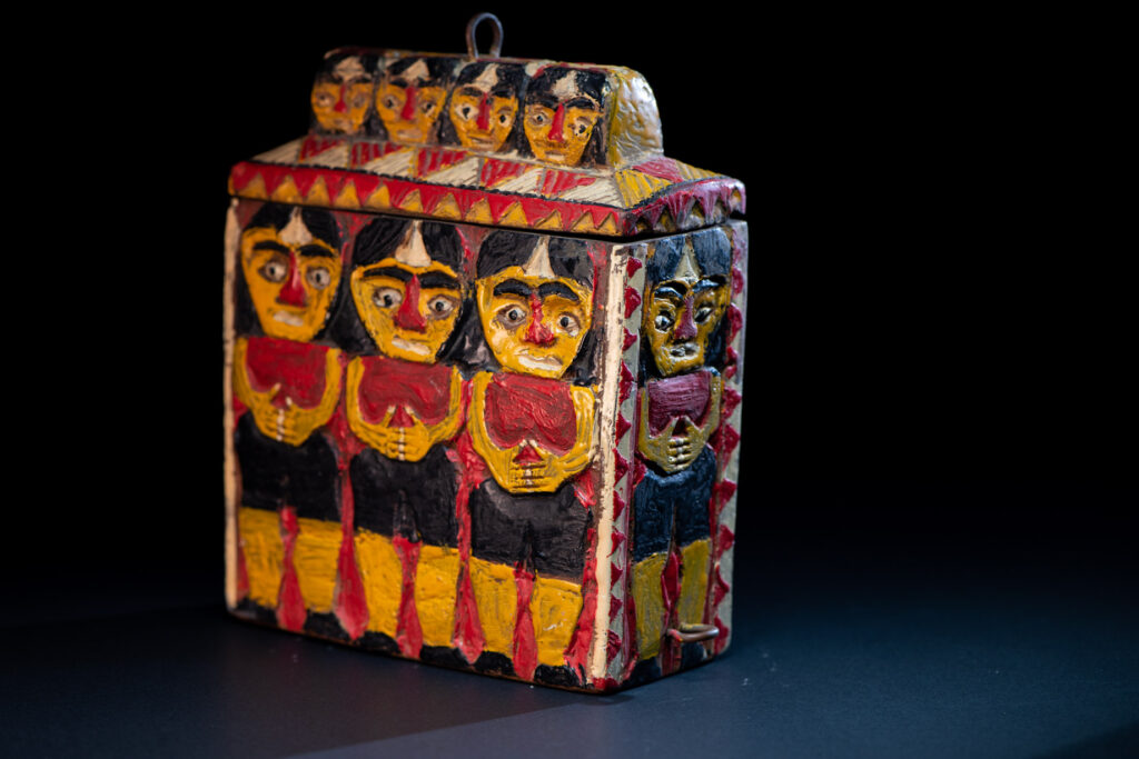 Paiwan tribe shaman box features a sliding lid, carved with human heads and painted in red, yellow, white, and black. Standing figure is carved on the other sides.
