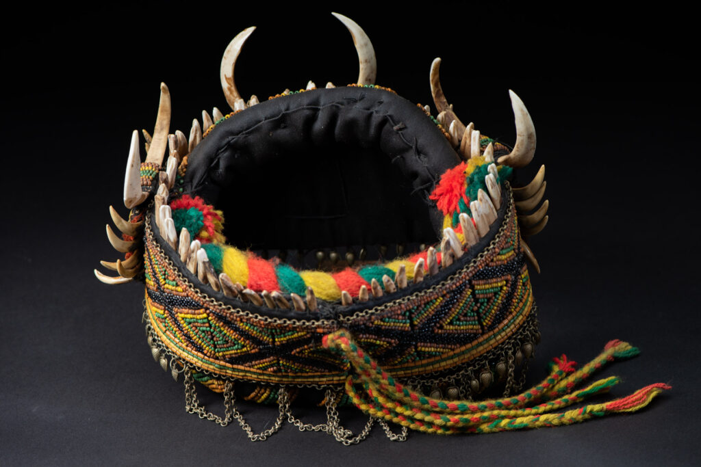 Women's headdress from the Paiwan tribe, made of green, yellow, red, and black beads arranged in geometric patterns, surrounded by chains and topped with boar tusks.