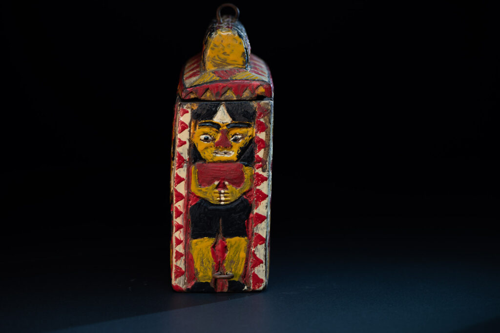 Paiwan tribe shaman box features a sliding lid, carved with human heads and painted in red, yellow, white, and black. Standing figure is carved on the other sides.