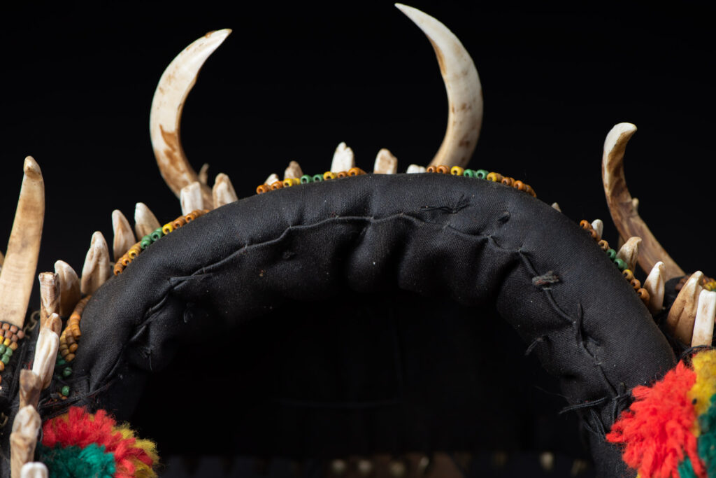 Women's headdress from the Paiwan tribe, made of green, yellow, red, and black beads arranged in geometric patterns, surrounded by chains and topped with boar tusks.