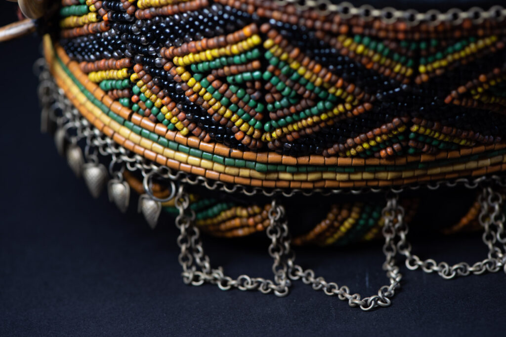 Women's headdress from the Paiwan tribe, made of green, yellow, red, and black beads arranged in geometric patterns, surrounded by chains and topped with boar tusks.