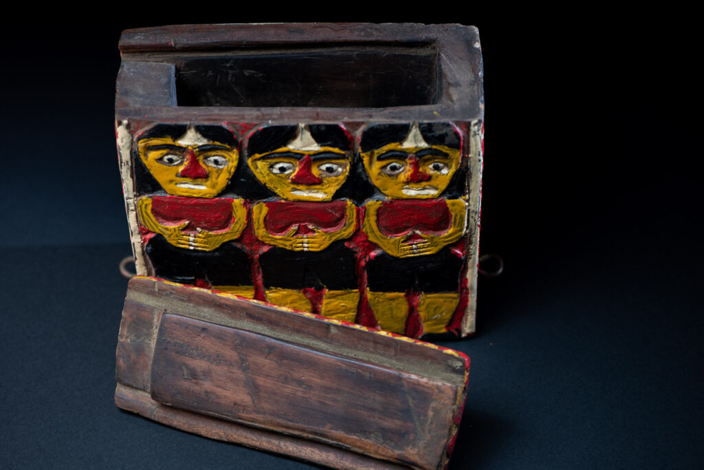 Paiwan tribe shaman box features a sliding lid, carved with human heads and painted in red, yellow, white, and black. Standing figure is carved on the other sides.