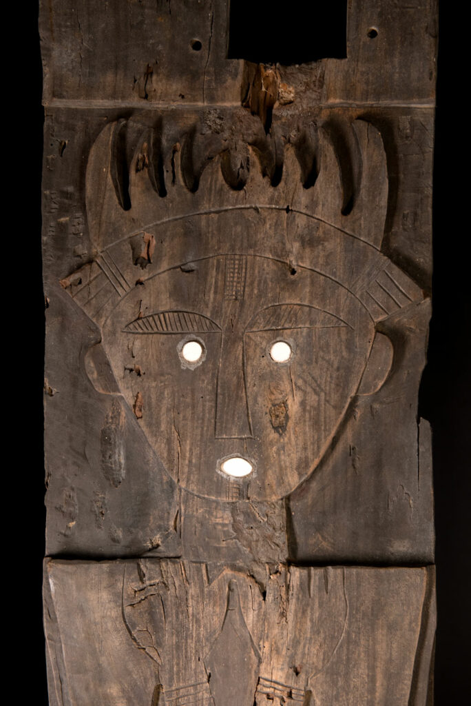 Pair of ancestor panels from the Paiwan tribe, depicting a male and a female figure, both wearing feathered headdresses — symbols of valor and vigor. The panels are inlaid with porcelain circles at the eyes, mouth, and waist, representing the ceremonial belts they wear.