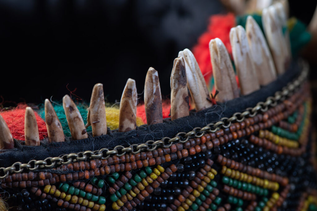 Women's headdress from the Paiwan tribe, made of green, yellow, red, and black beads arranged in geometric patterns, surrounded by chains and topped with boar tusks.