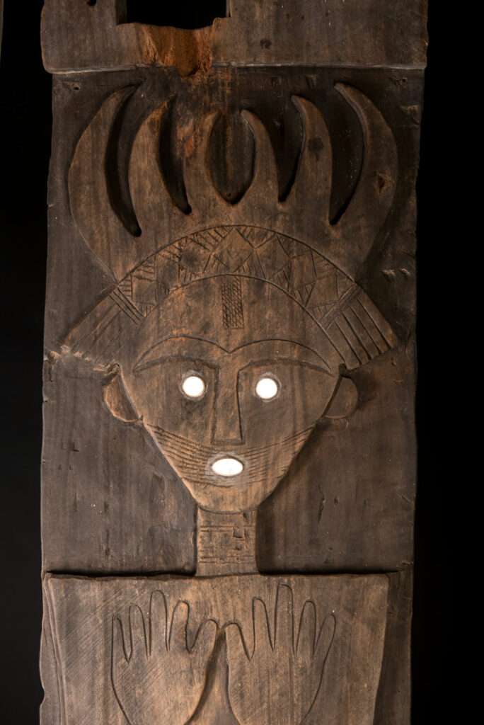 Pair of ancestor panels from the Paiwan tribe, depicting a male and a female figure, both wearing feathered headdresses — symbols of valor and vigor. The panels are inlaid with porcelain circles at the eyes, mouth, and waist, representing the ceremonial belts they wear.