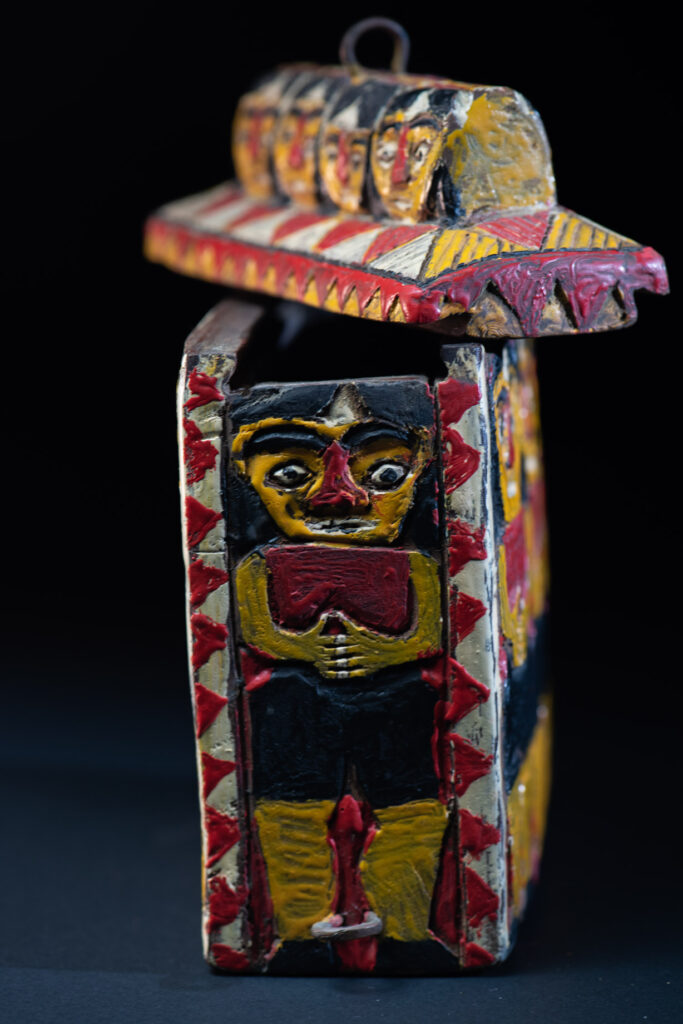 Paiwan tribe shaman box features a sliding lid, carved with human heads and painted in red, yellow, white, and black. Standing figure is carved on the other sides.