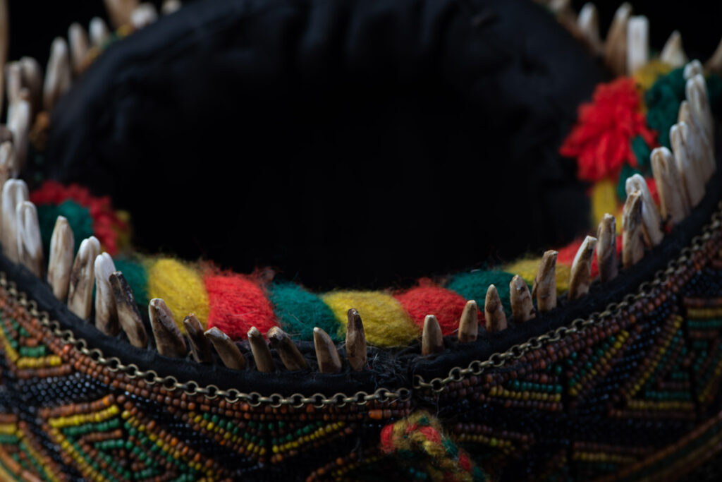 Women's headdress from the Paiwan tribe, made of green, yellow, red, and black beads arranged in geometric patterns, surrounded by chains and topped with boar tusks.