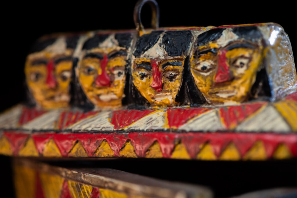 Paiwan tribe shaman box features a sliding lid, carved with human heads and painted in red, yellow, white, and black. Standing figure is carved on the other sides.