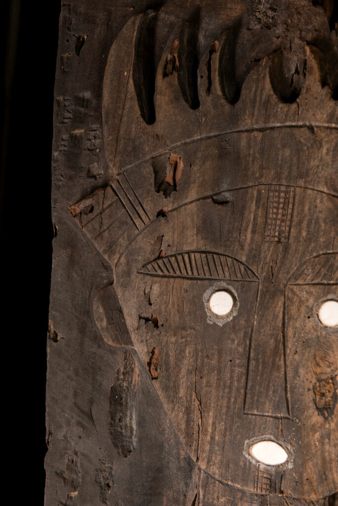 Pair of ancestor panels from the Paiwan tribe, depicting a male and a female figure, both wearing feathered headdresses — symbols of valor and vigor. The panels are inlaid with porcelain circles at the eyes, mouth, and waist, representing the ceremonial belts they wear.