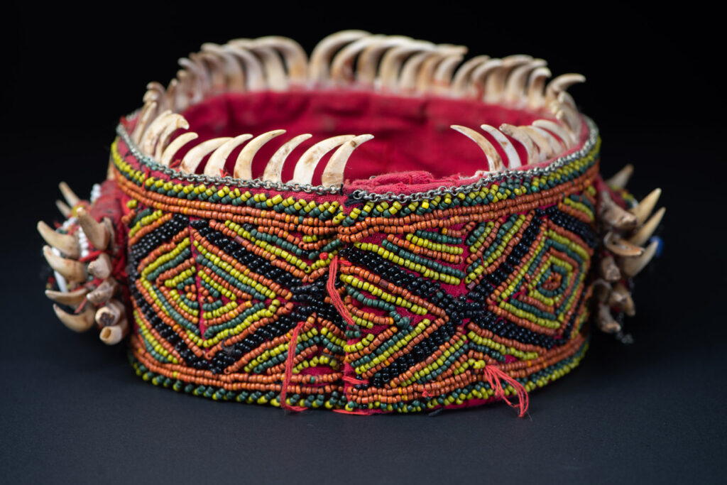 Women's headdress from the Paiwan tribe, made of green, yellow, red, and black beads arranged in geometric patterns, and topped with boar tusks.