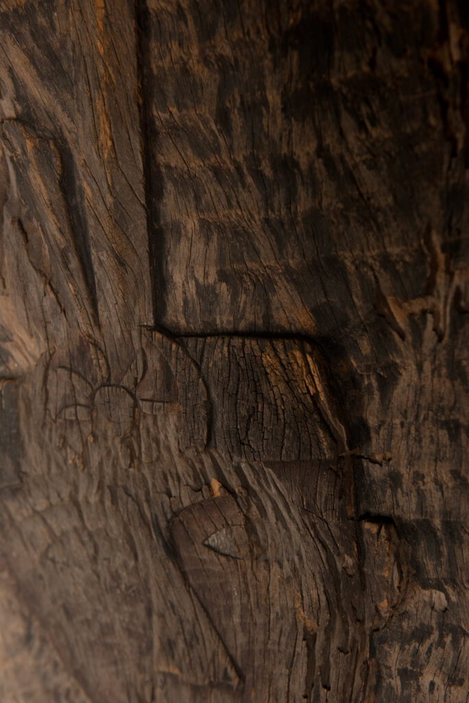Old ancestor panel from the Paiwan tribe, carved with a standing warrior, one hand resting on his rifle and the other on the pommel of his sword. He is dressed in ceremonial attire and wears a hat adorned with eagle feathers, a symbol of valor.