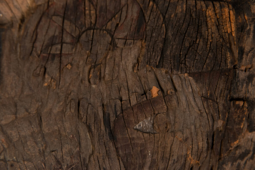 Old ancestor panel from the Paiwan tribe, carved with a standing warrior, one hand resting on his rifle and the other on the pommel of his sword. He is dressed in ceremonial attire and wears a hat adorned with eagle feathers, a symbol of valor.