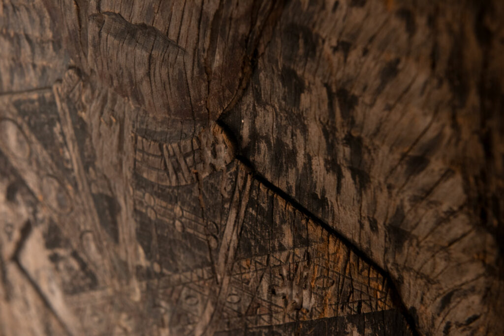 Old ancestor panel from the Paiwan tribe, carved with a standing warrior, one hand resting on his rifle and the other on the pommel of his sword. He is dressed in ceremonial attire and wears a hat adorned with eagle feathers, a symbol of valor.