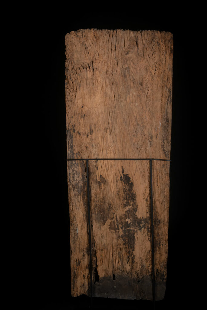 Old ancestor panel from the Paiwan tribe, carved with a standing warrior, one hand resting on his rifle and the other on the pommel of his sword. He is dressed in ceremonial attire and wears a hat adorned with eagle feathers, a symbol of valor.