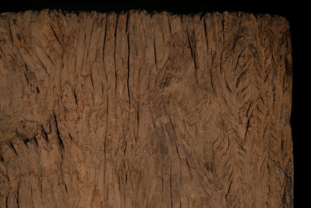 Old ancestor panel from the Paiwan tribe, carved with a standing warrior, one hand resting on his rifle and the other on the pommel of his sword. He is dressed in ceremonial attire and wears a hat adorned with eagle feathers, a symbol of valor.