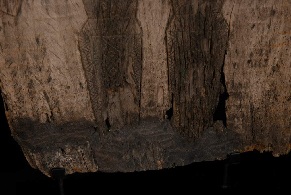 Old ancestor panel from the Paiwan tribe, carved with a standing warrior, one hand resting on his rifle and the other on the pommel of his sword. He is dressed in ceremonial attire and wears a hat adorned with eagle feathers, a symbol of valor.