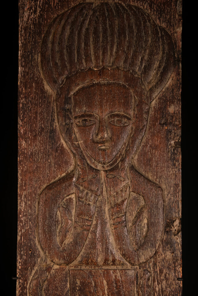 Ancestor panel from the Paiwan tribe, carved with a figure wearing a hat adorned with eagle feathers, a symbol of valor. His face is encircled by two snakes merging into one, and flanked by two additional sacred snakes on each side.