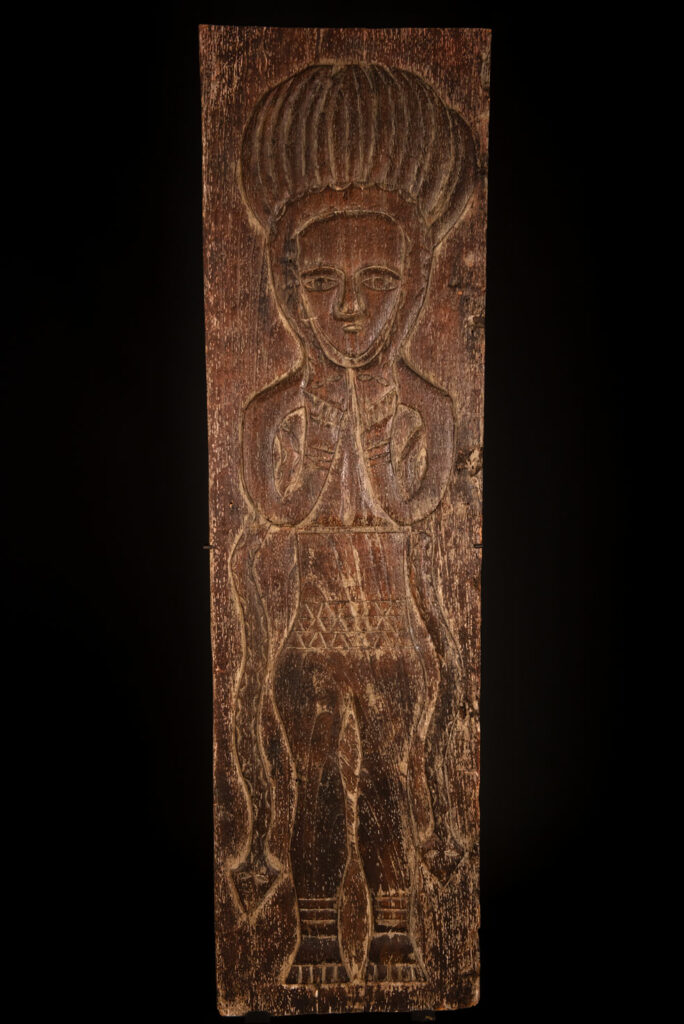 Ancestor panel from the Paiwan tribe, carved with a figure wearing a hat adorned with eagle feathers, a symbol of valor. His face is encircled by two snakes merging into one, and flanked by two additional sacred snakes on each side.