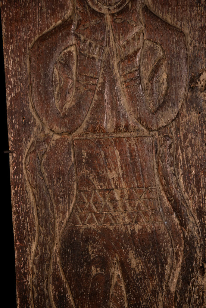 Ancestor panel from the Paiwan tribe, carved with a figure wearing a hat adorned with eagle feathers, a symbol of valor. His face is encircled by two snakes merging into one, and flanked by two additional sacred snakes on each side.