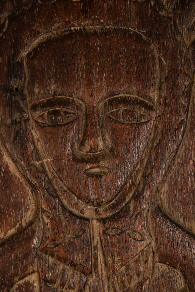 Ancestor panel from the Paiwan tribe, carved with a figure wearing a hat adorned with eagle feathers, a symbol of valor. His face is encircled by two snakes merging into one, and flanked by two additional sacred snakes on each side.