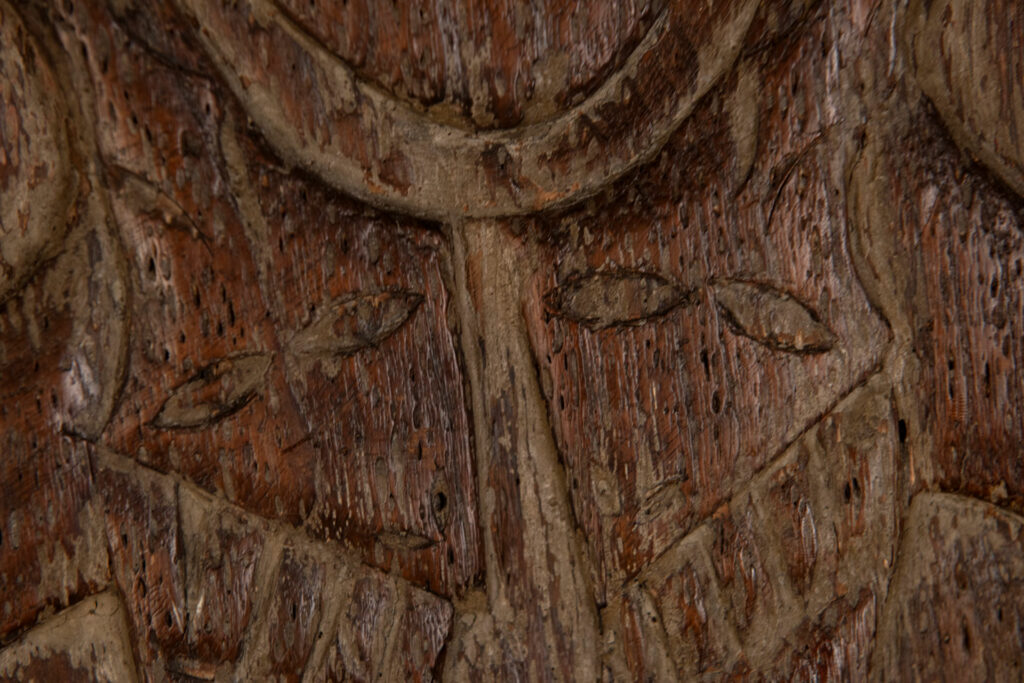 Ancestor panel from the Paiwan tribe, carved with a figure wearing a hat adorned with eagle feathers, a symbol of valor. His face is encircled by two snakes merging into one, and flanked by two additional sacred snakes on each side.