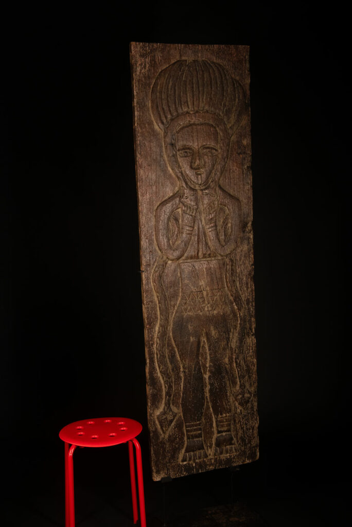 Ancestor panel from the Paiwan tribe, carved with a figure wearing a hat adorned with eagle feathers, a symbol of valor. His face is encircled by two snakes merging into one, and flanked by two additional sacred snakes on each side.