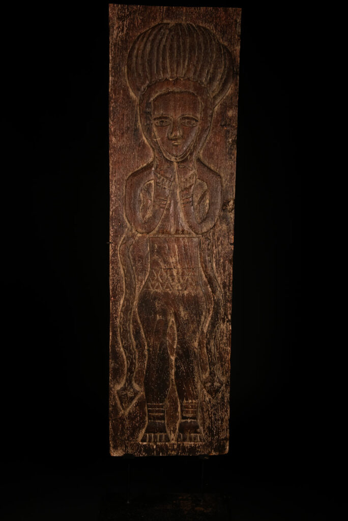 Ancestor panel from the Paiwan tribe, carved with a figure wearing a hat adorned with eagle feathers, a symbol of valor. His face is encircled by two snakes merging into one, and flanked by two additional sacred snakes on each side.