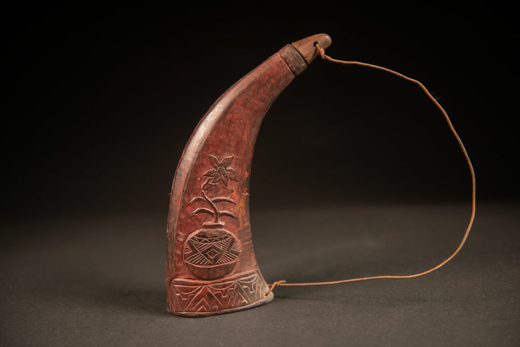 Powder flask from the Rukai tribe, made from a horn sealed at the base with a wooden plug. the body is carved on 2 sides and tint in red .