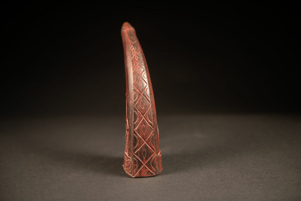 Powder flask from the Rukai tribe, made from a horn sealed at the base with a wooden plug. the body is carved on 2 sides and tint in red .