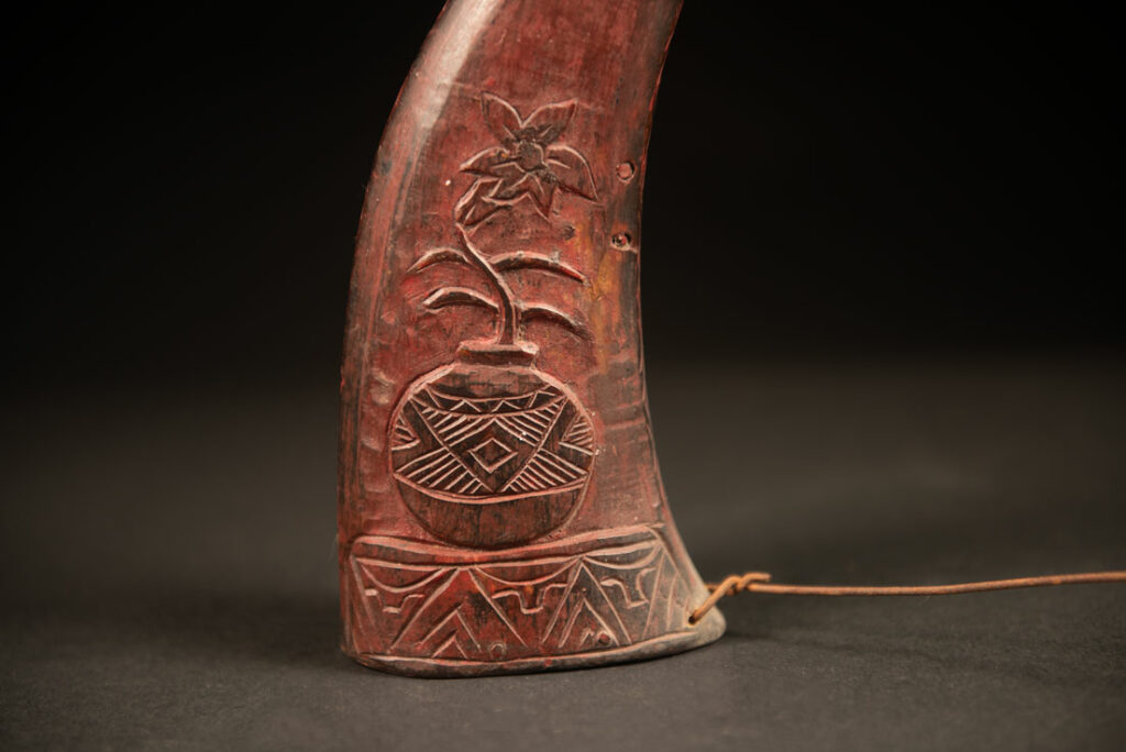 Powder flask from the Rukai tribe, made from a horn sealed at the base with a wooden plug. the body is carved on 2 sides and tint in red .