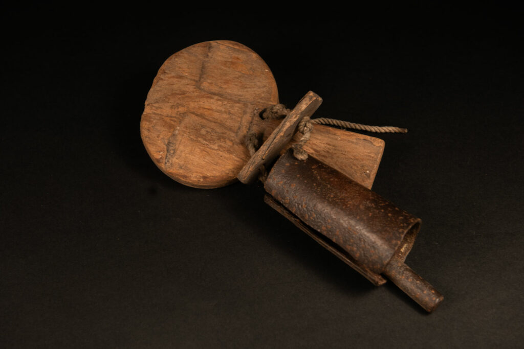 Rukai tribe alarm bell showing a wooden handle shaped with a human face linked with a cylindrical bell .