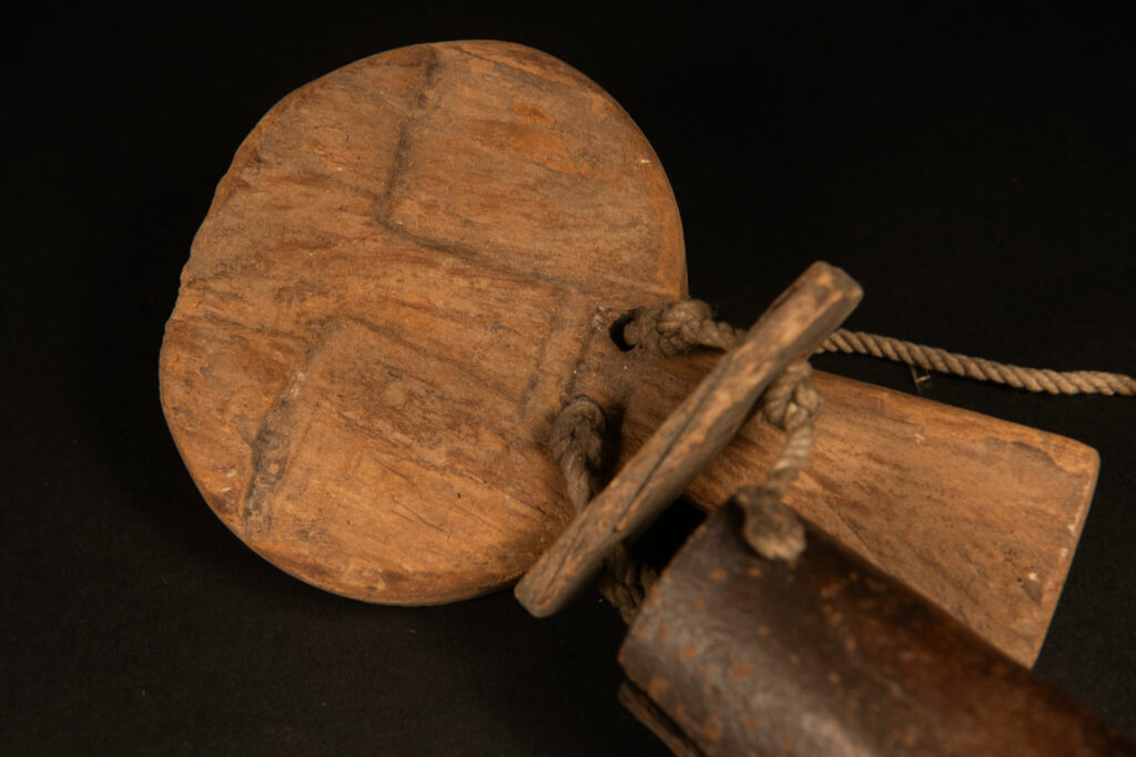 Rukai tribe alarm bell showing a wooden handle shaped with a human face linked with a cylindrical bell .